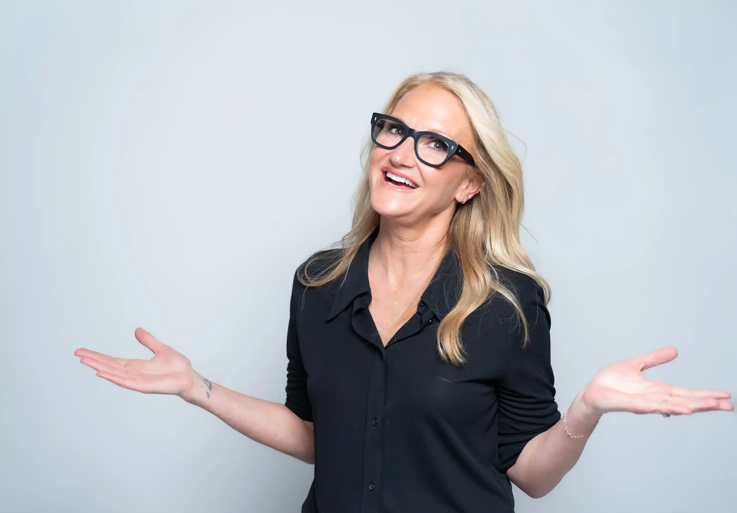 Mel Robbins smiling with hands up in shrug gesture on grey background