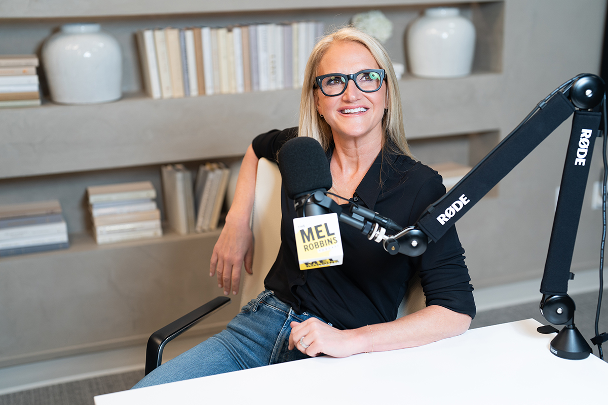 Mel Robbins sitting in front of microphone in recording studio, smiling