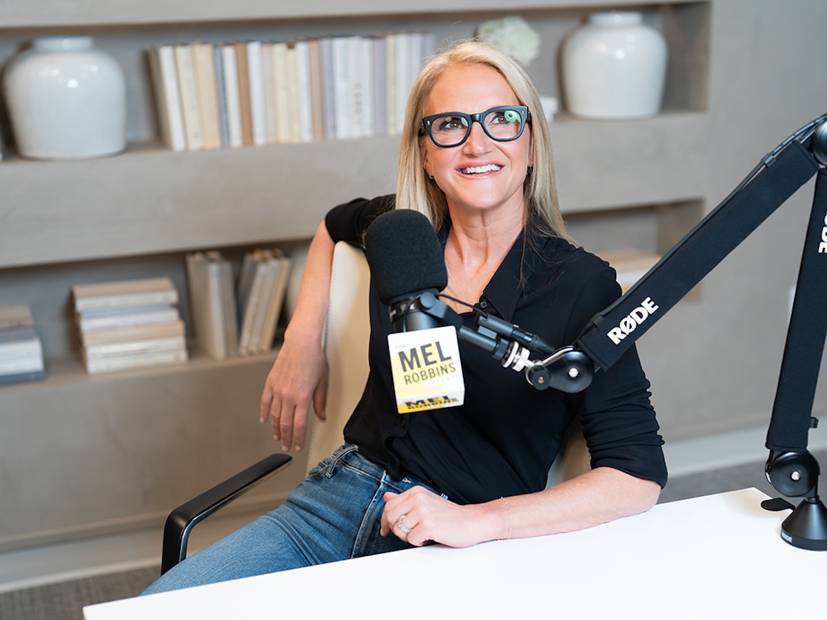 Mel Robbins sitting in front of microphone in recording studio, smiling